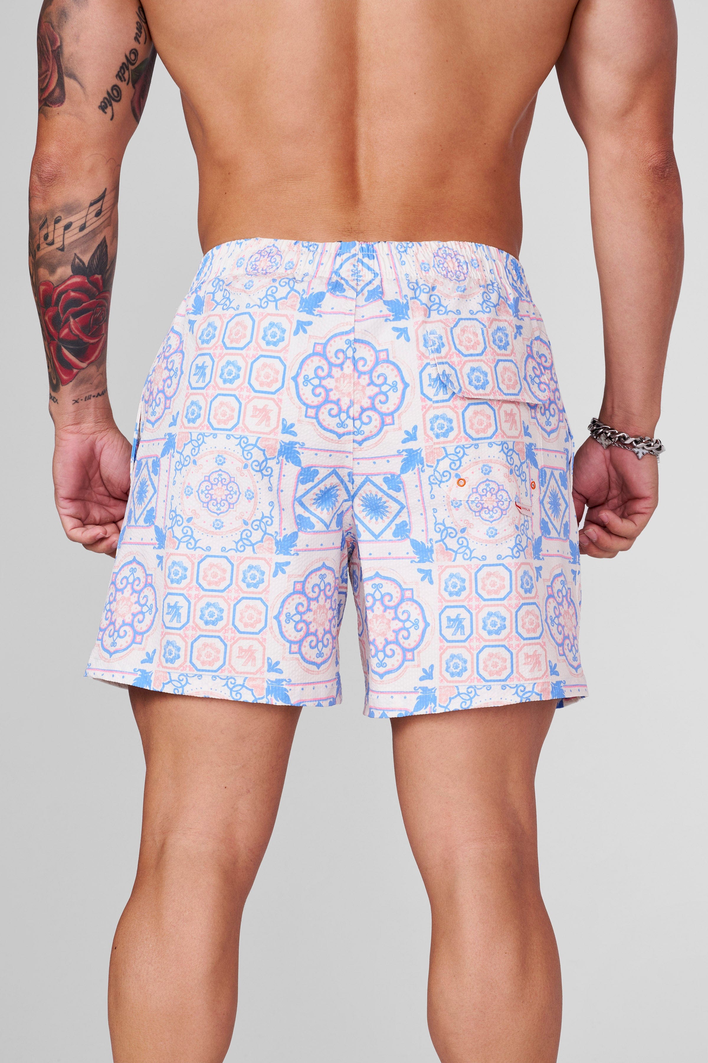 Model wearing mens printed swim shorts by a tropical pool