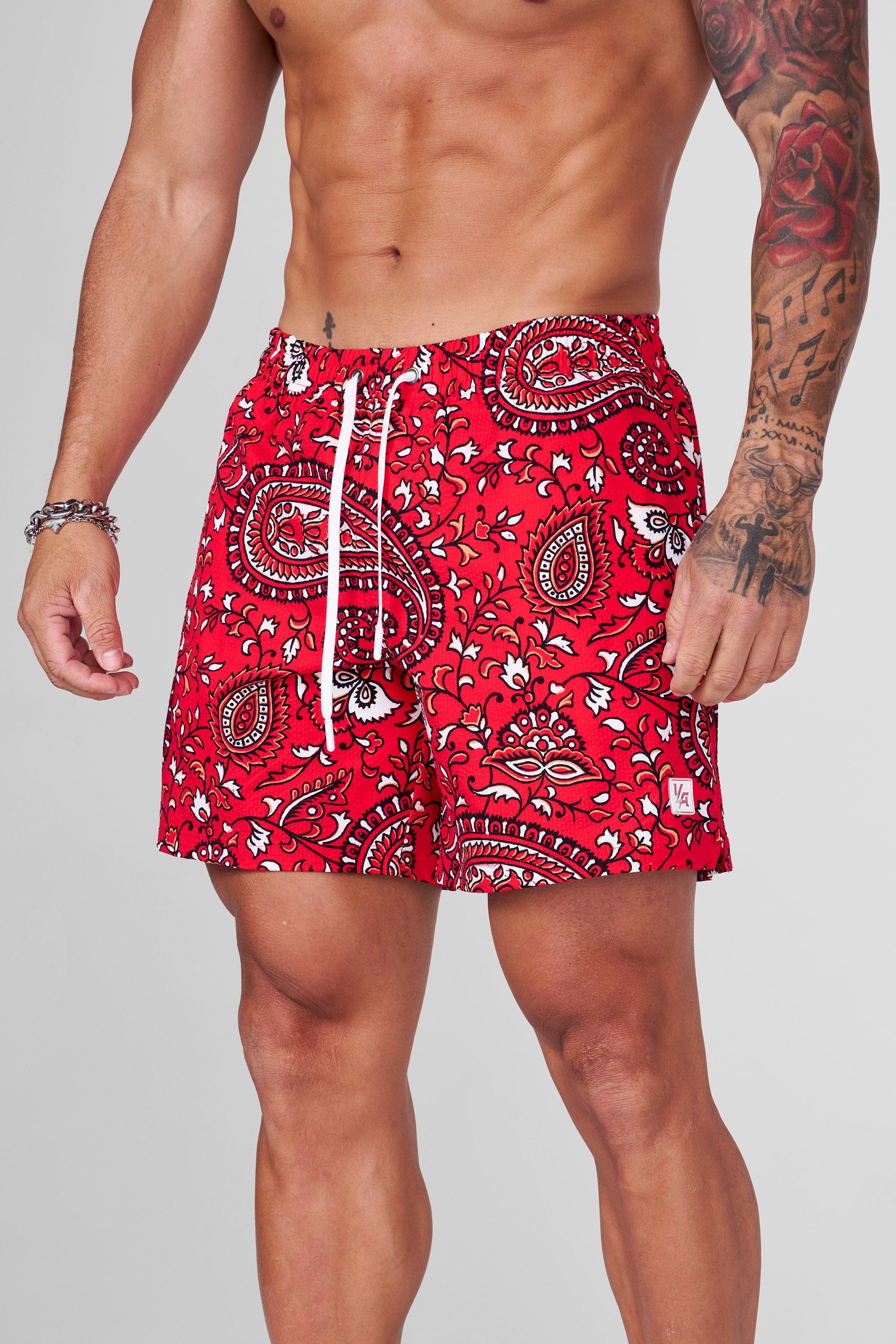 Model wearing mens printed swim shorts by a tropical pool