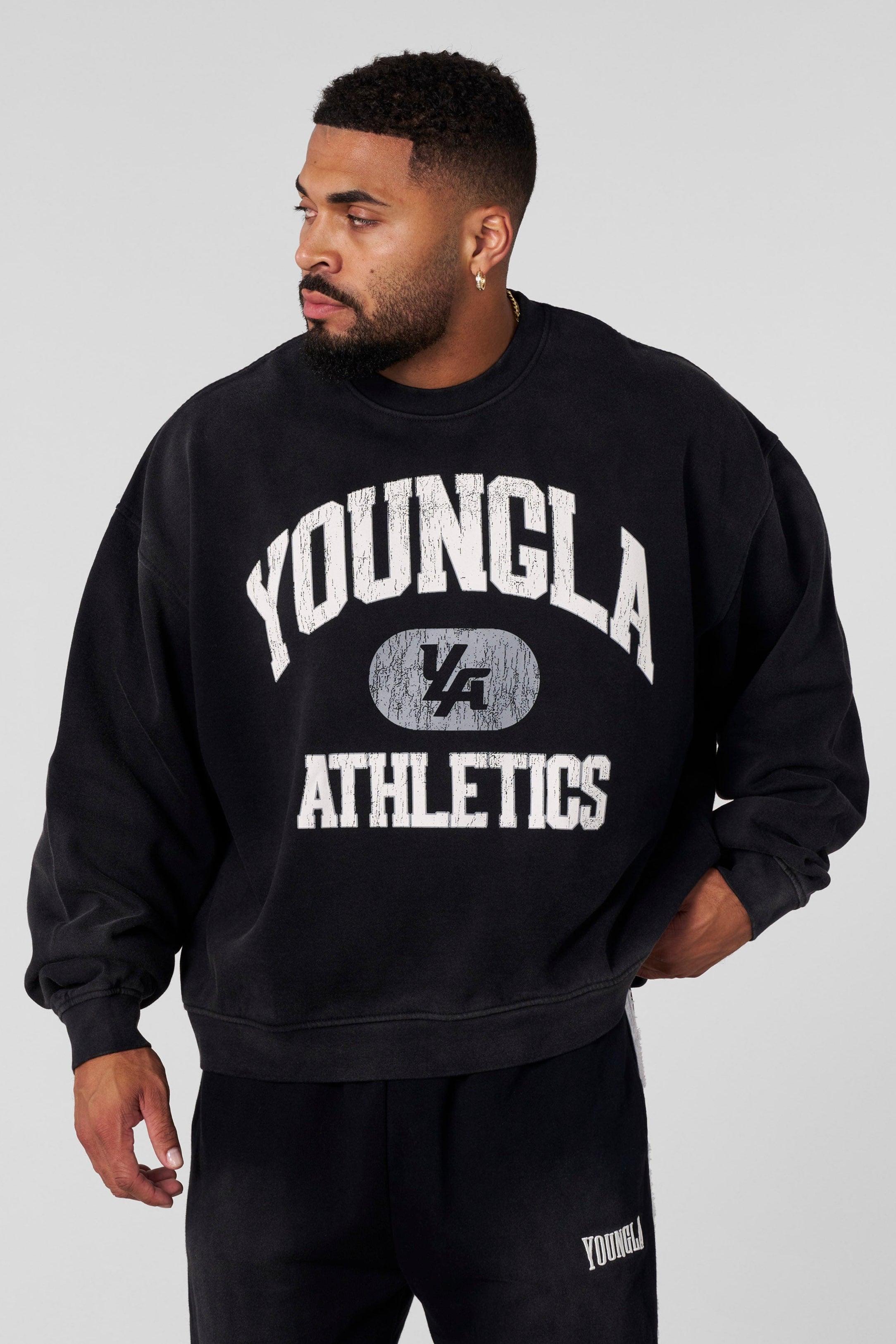 Front angle of model wearing oversized black crewneck with varsity print in urban setting