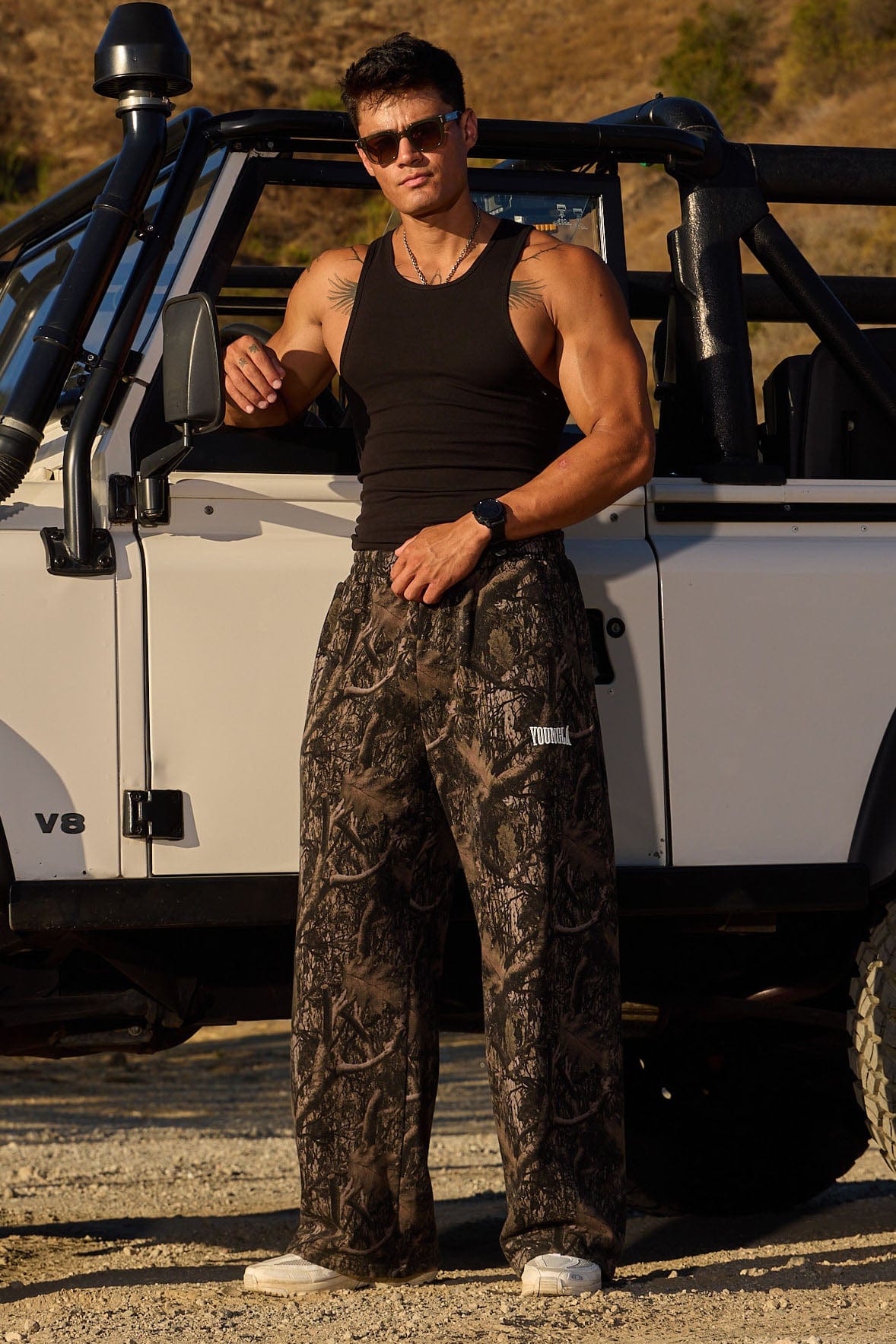 Model wearing YOUNGLA baggy camo sweatpants in a casual setting.