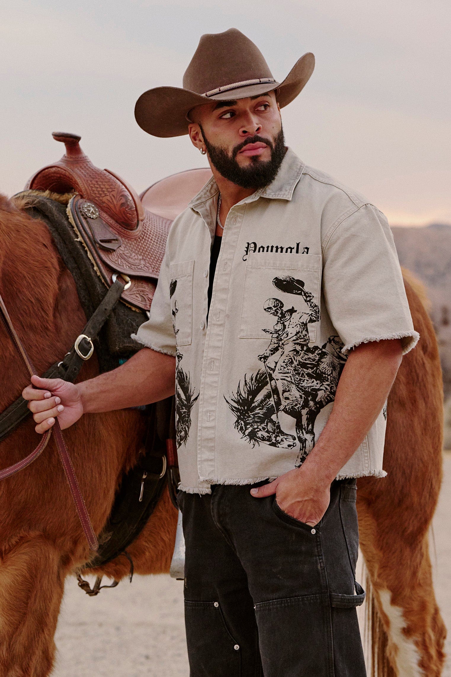 Model wearing western style shirt standing near wooden fence